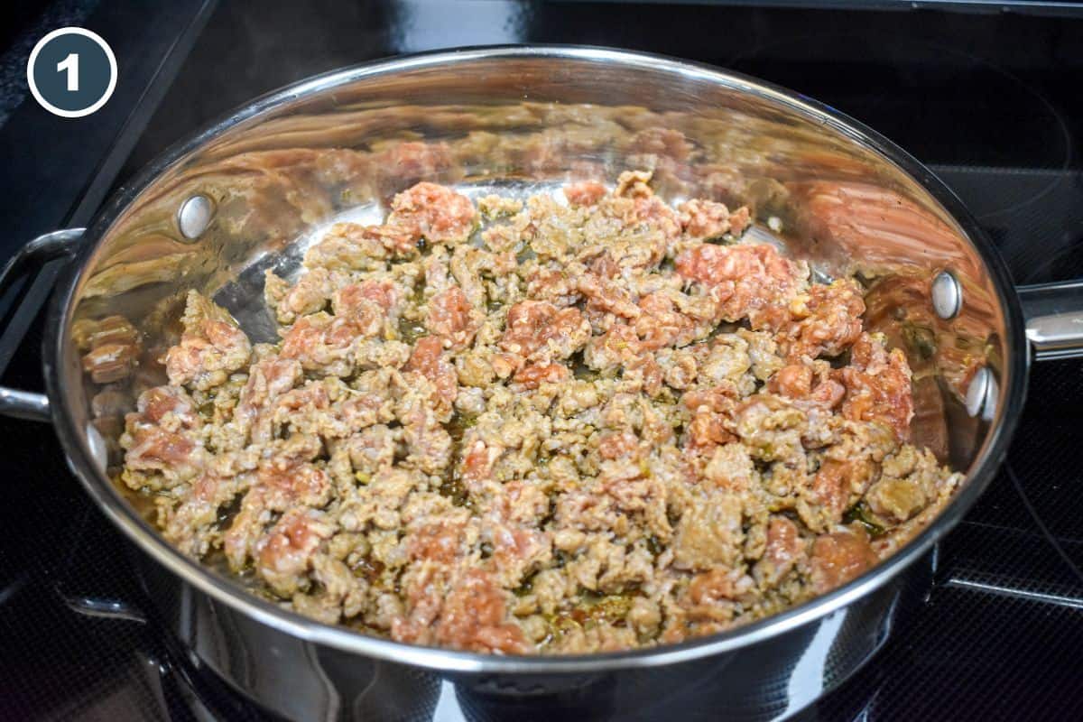 Browned crumbled Italian sausage in a stainless steel skillet on a stovetop.