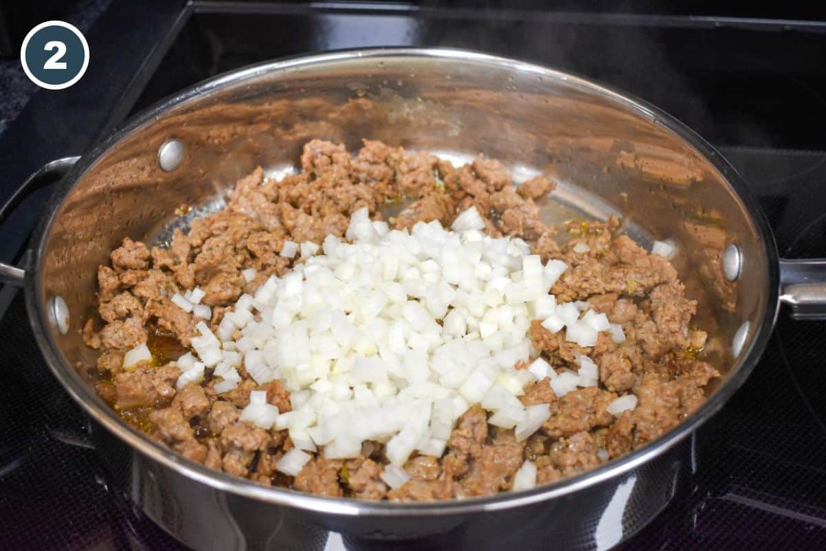 Diced white onion added on top of browned sausage in a stainless steel skillet.