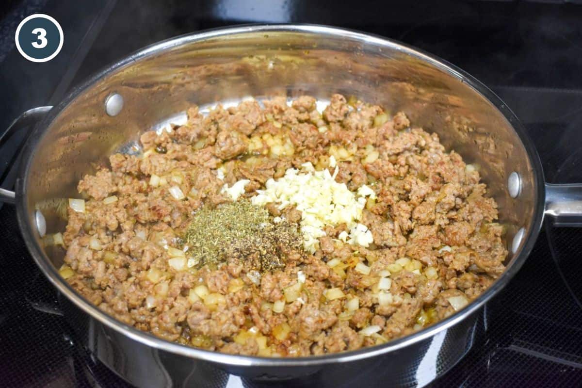 Minced garlic, Italian seasoning, and black pepper on top of browned sausage and onion in a skillet.