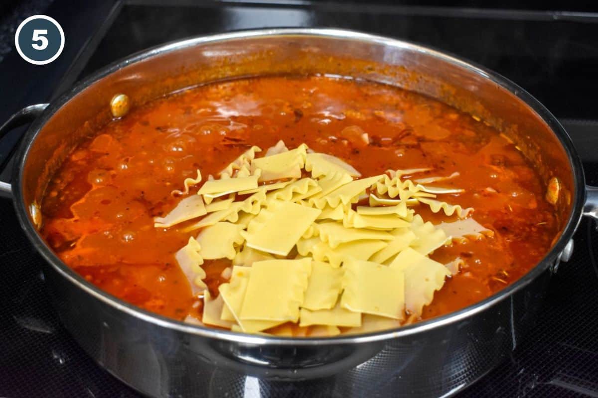 Broken lasagna noodles added to simmering tomato sauce in a large stainless steel skillet.