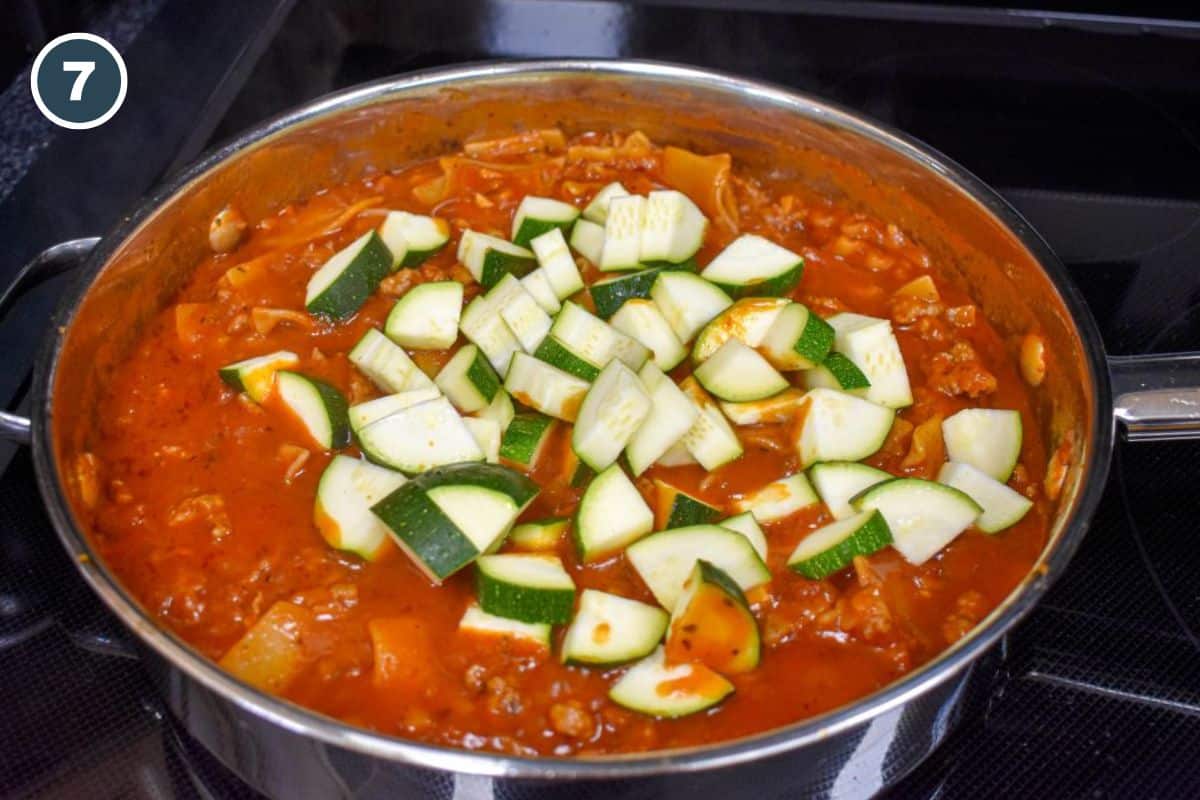 Chopped zucchini added to the simmering lasagna noodles and tomato sauce in a skillet.
