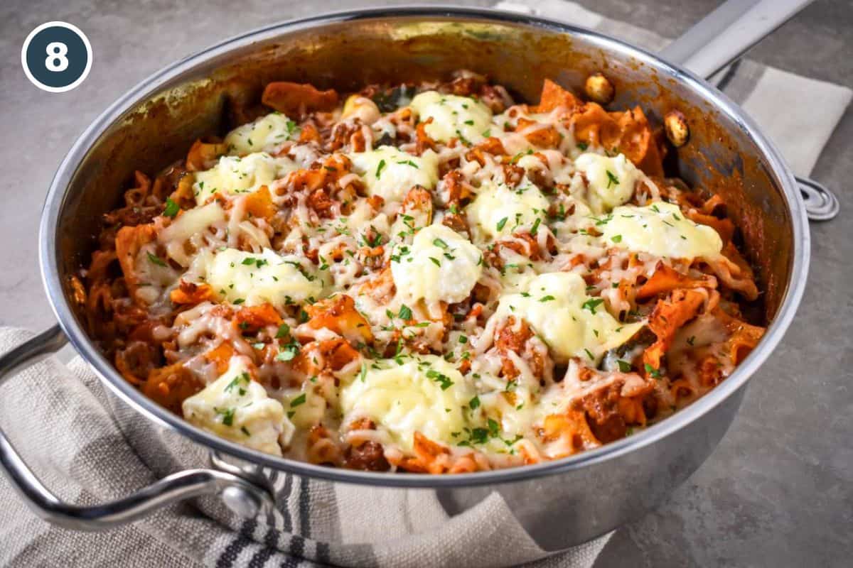 Finished skillet lasagna in a stainless steel pan, topped with melted ricotta, mozzarella, and chopped fresh parsley.