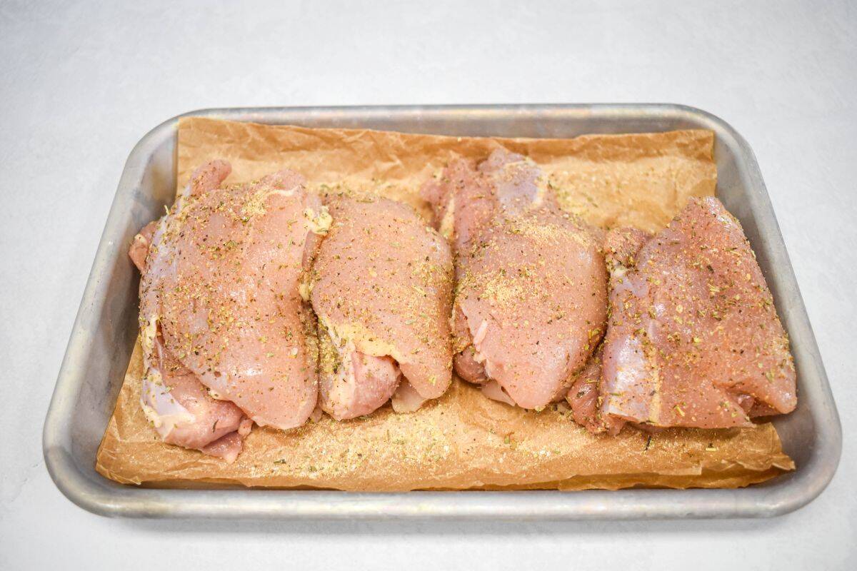 Raw chicken thighs are seasoned with salt, pepper, garlic powder, onion powder, and Italian seasoning on a tray.