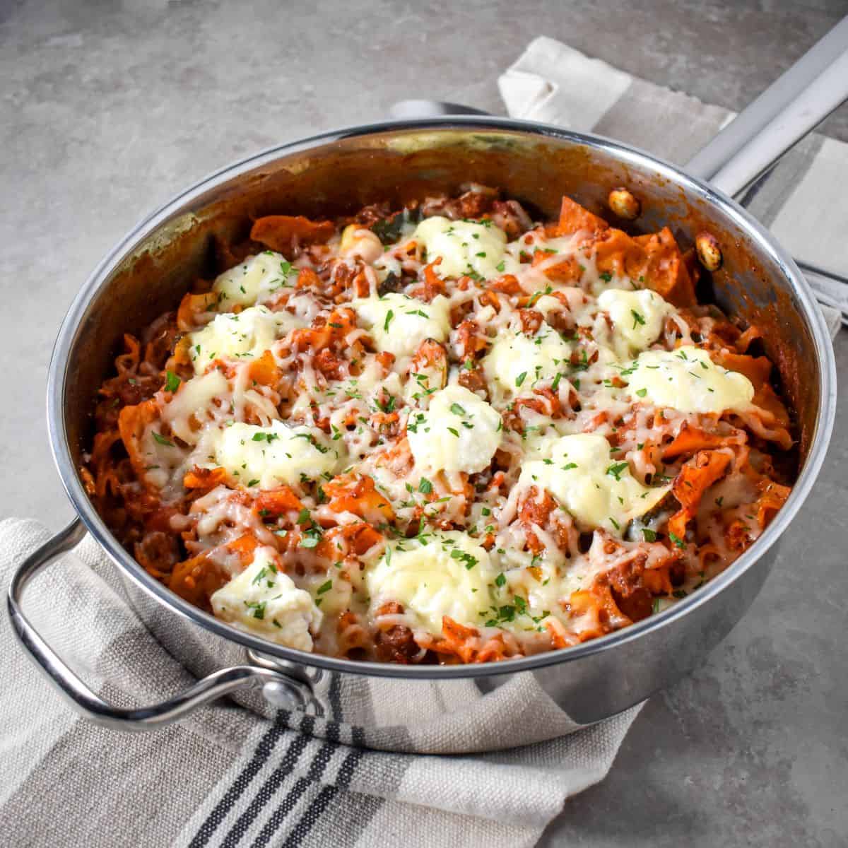 One-pan skillet lasagna topped with melted mozzarella and dollops of ricotta, garnished with herbs, ready to serve.