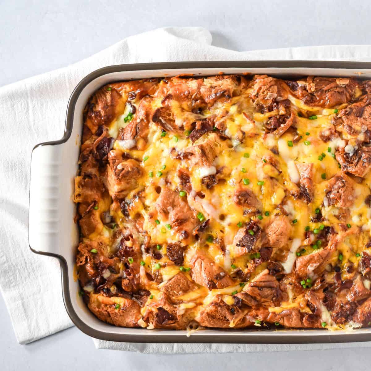 Bacon croissant breakfast casserole baked golden with melted cheese and crispy bacon in a baking dish.