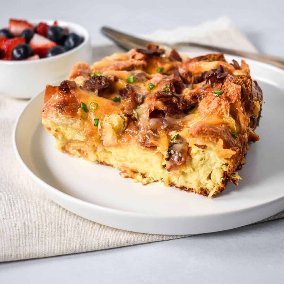 Close-up of bacon croissant breakfast casserole slice showing custardy center and crispy bacon on top.