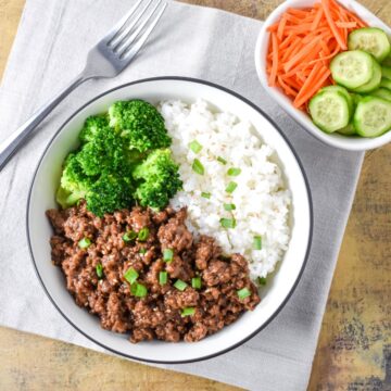 Ground beef bowl with rice, broccoli, and green onions served with fresh vegetables on the side.