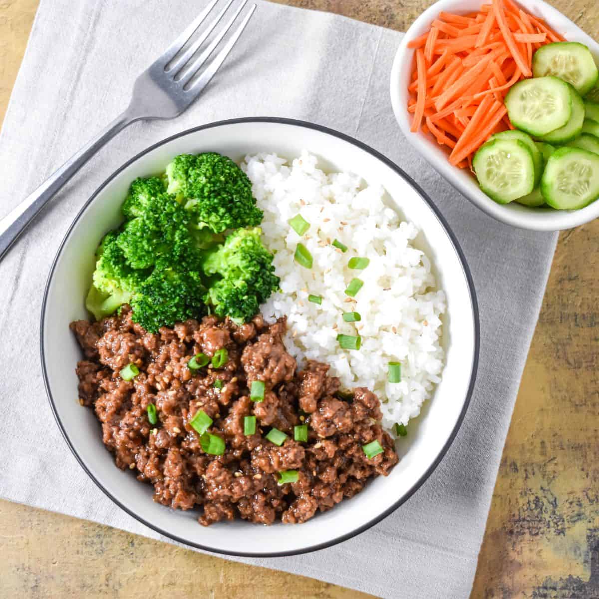 Ground beef bowl with rice, broccoli, and green onions served with fresh vegetables on the side.