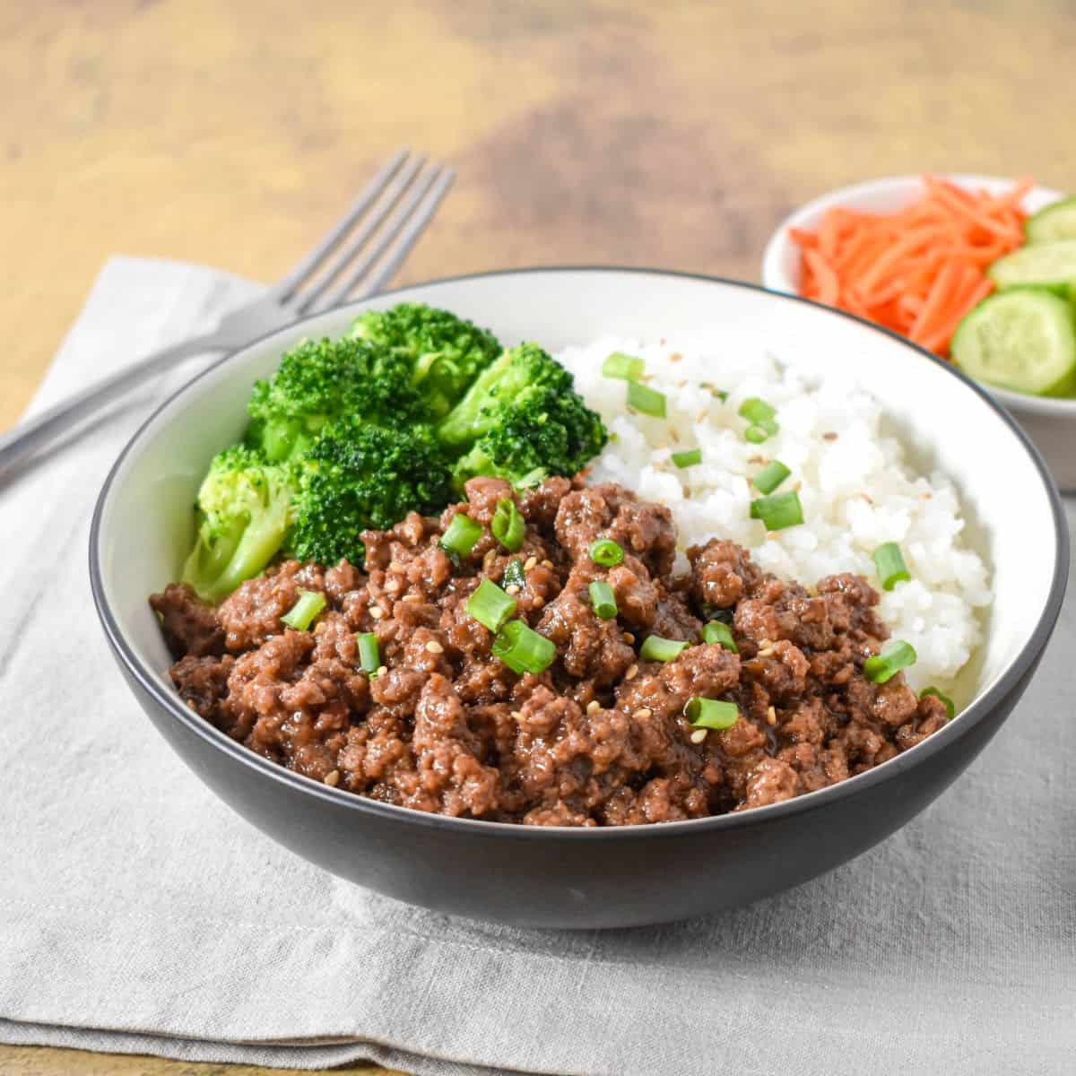 Ground beef bowl with rice and broccoli, served in a black and white bowl.