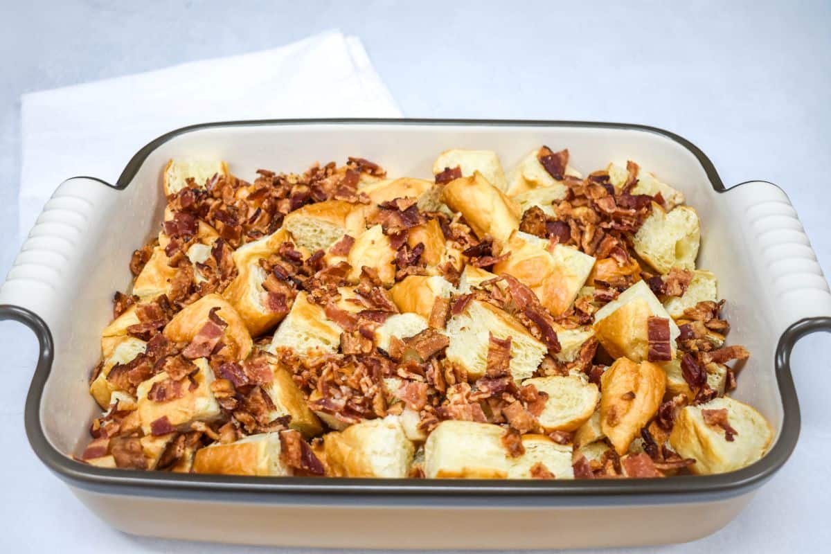 Chopped crispy bacon sprinkled evenly over the croissant pieces.