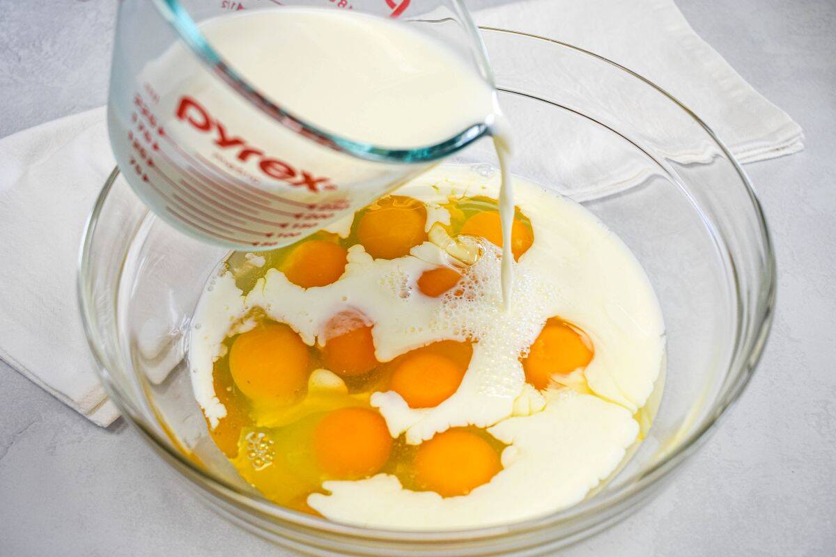Milk, being poured over eggs in a large, glass bowl to make the custard.