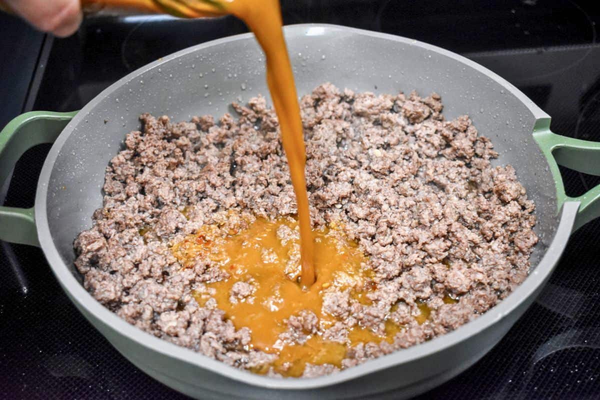 Pouring stir fry sauce over cooked ground beef in a skillet.