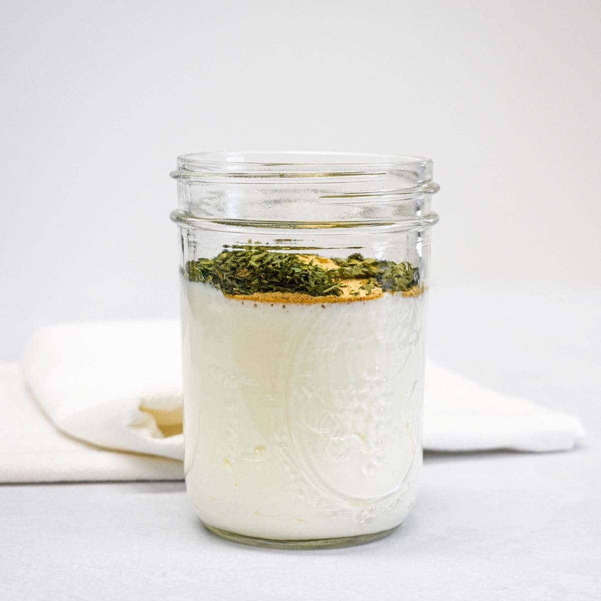 Ingredients for ranch dressing layered in a glass jar before mixing.