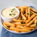 Bowl of creamy garlic aioli served with seasoned French fries on a white plate.