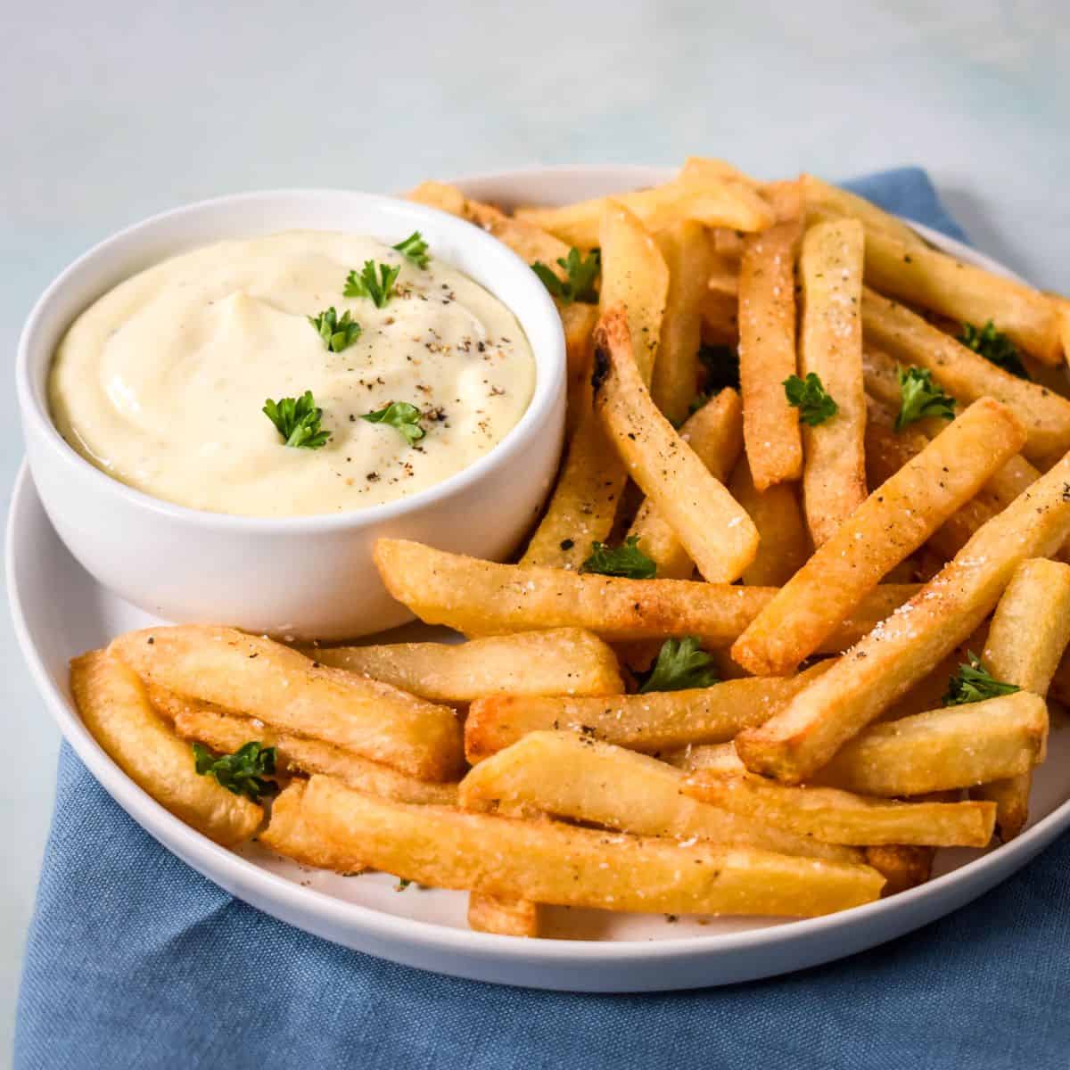Bowl of creamy garlic aioli served with seasoned French fries on a white plate.