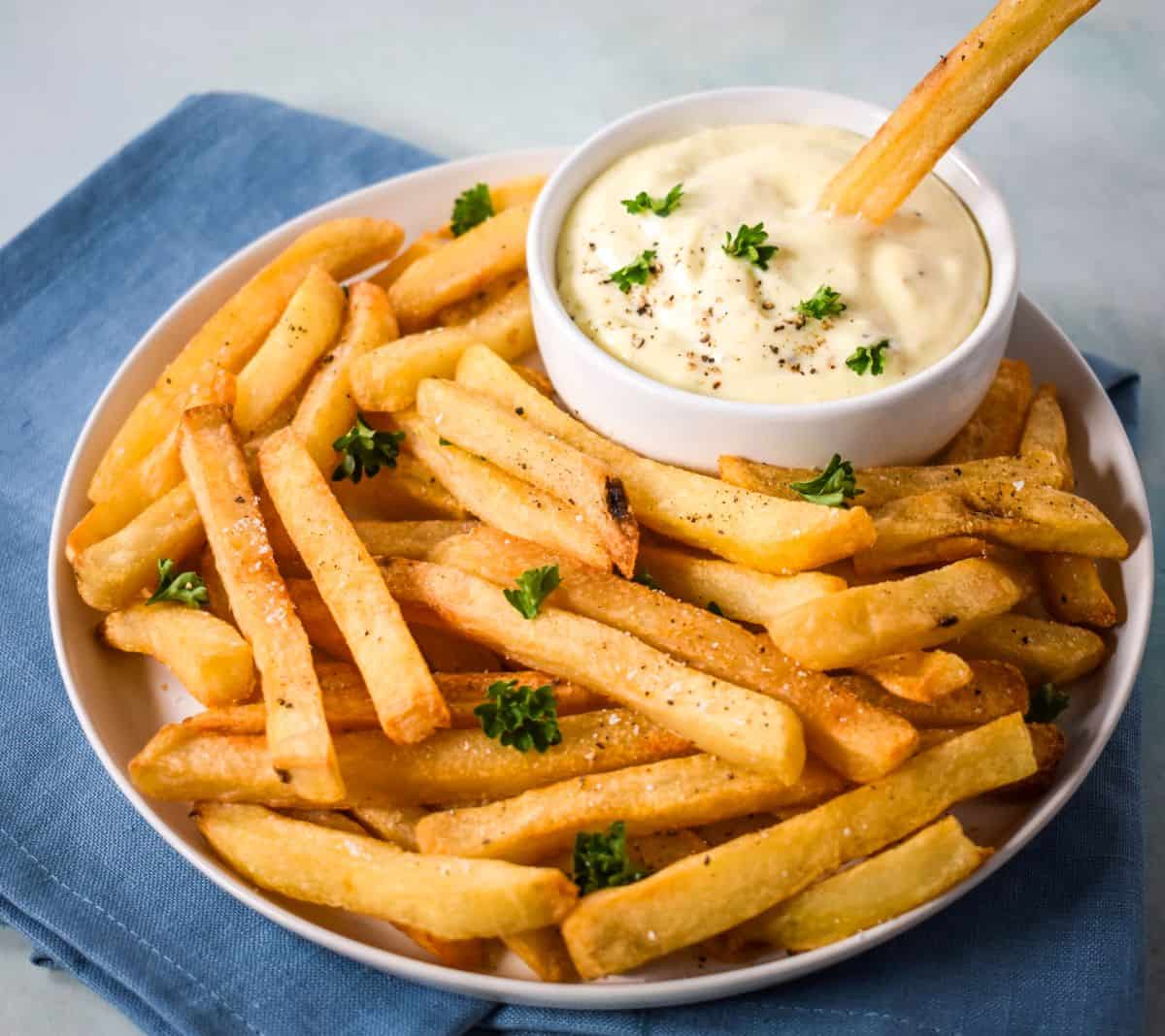 French fries served with a creamy dipping sauce and a fry dipped into the sauce.