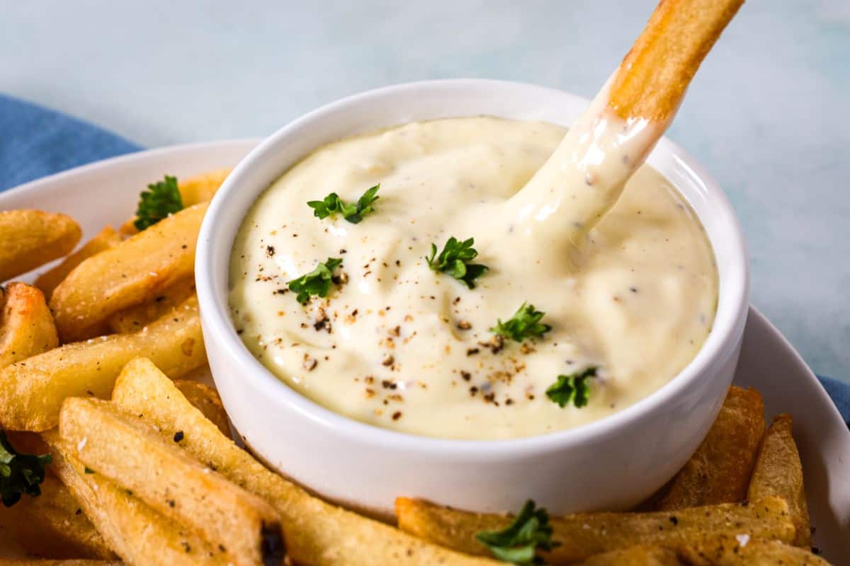 Close up of creamy aioli dip served with crispy fries and parsley garnish.