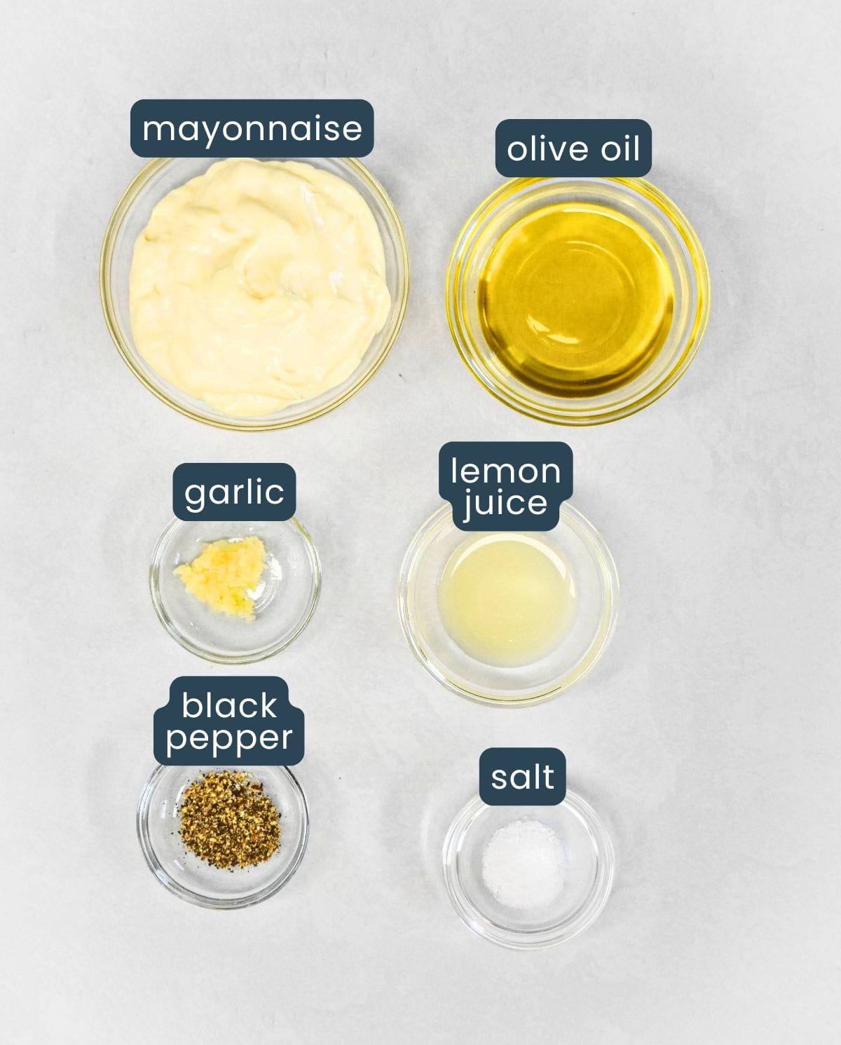 Ingredients needed to make homemade aioli including mayonnaise, olive oil, garlic, lemon juice, salt, and black pepper.