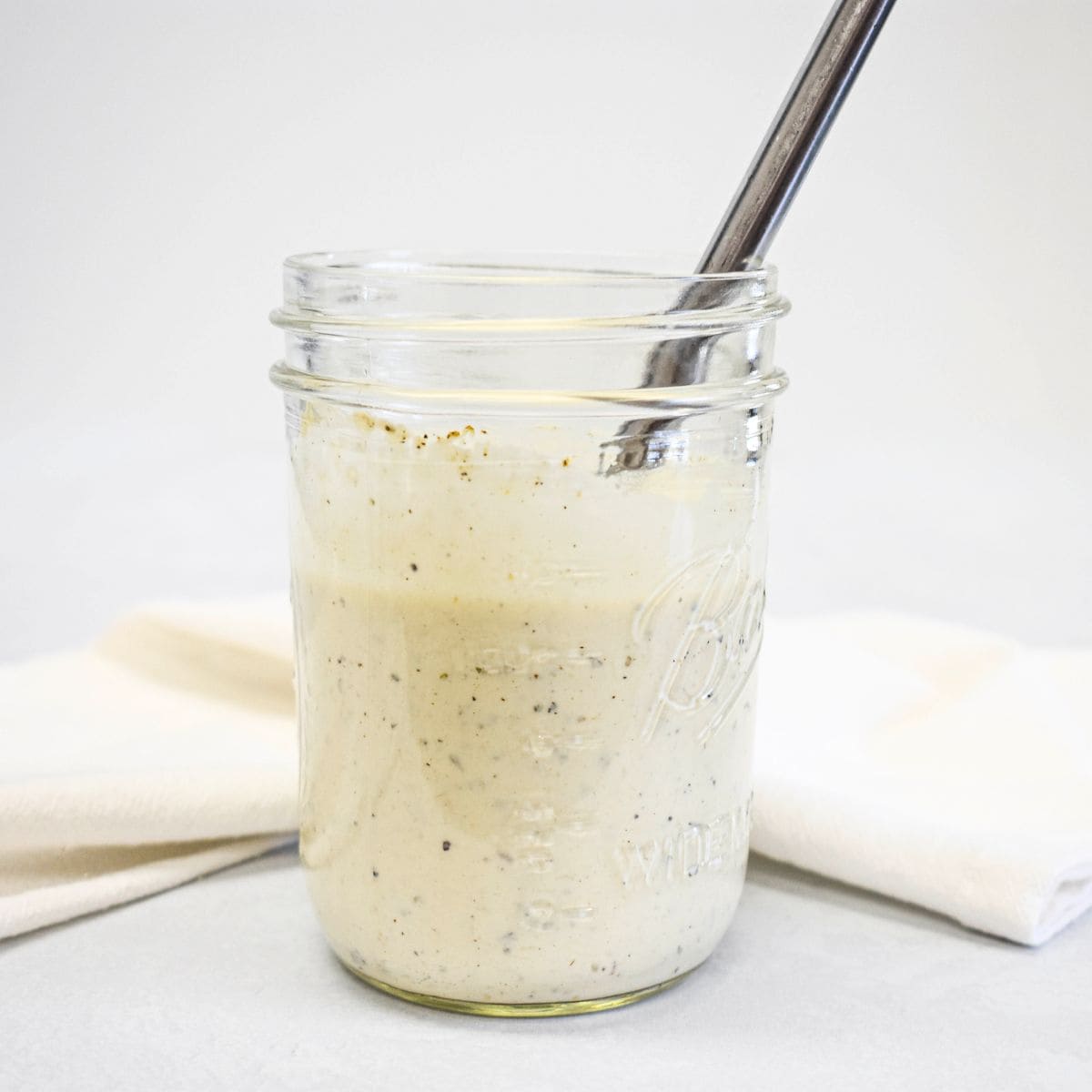 Mixed parmesan peppercorn dressing in a glass jar with visible black pepper and a spoon.