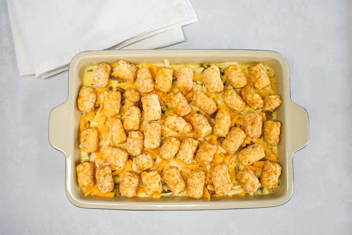 Frozen tater tots arranged on top of the breakfast casserole before baking.