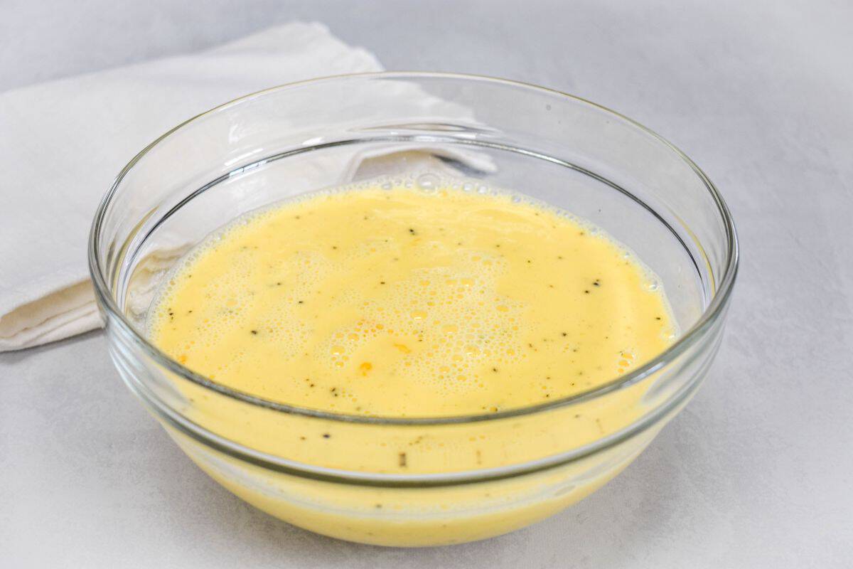 Eggs, milk, salt, and pepper whisked together in a glass mixing bowl.