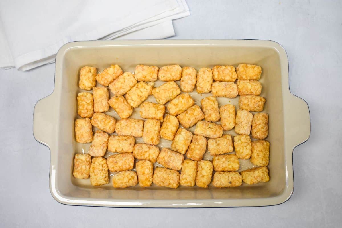 Frozen tater tots arranged in a single layer in a greased baking dish.