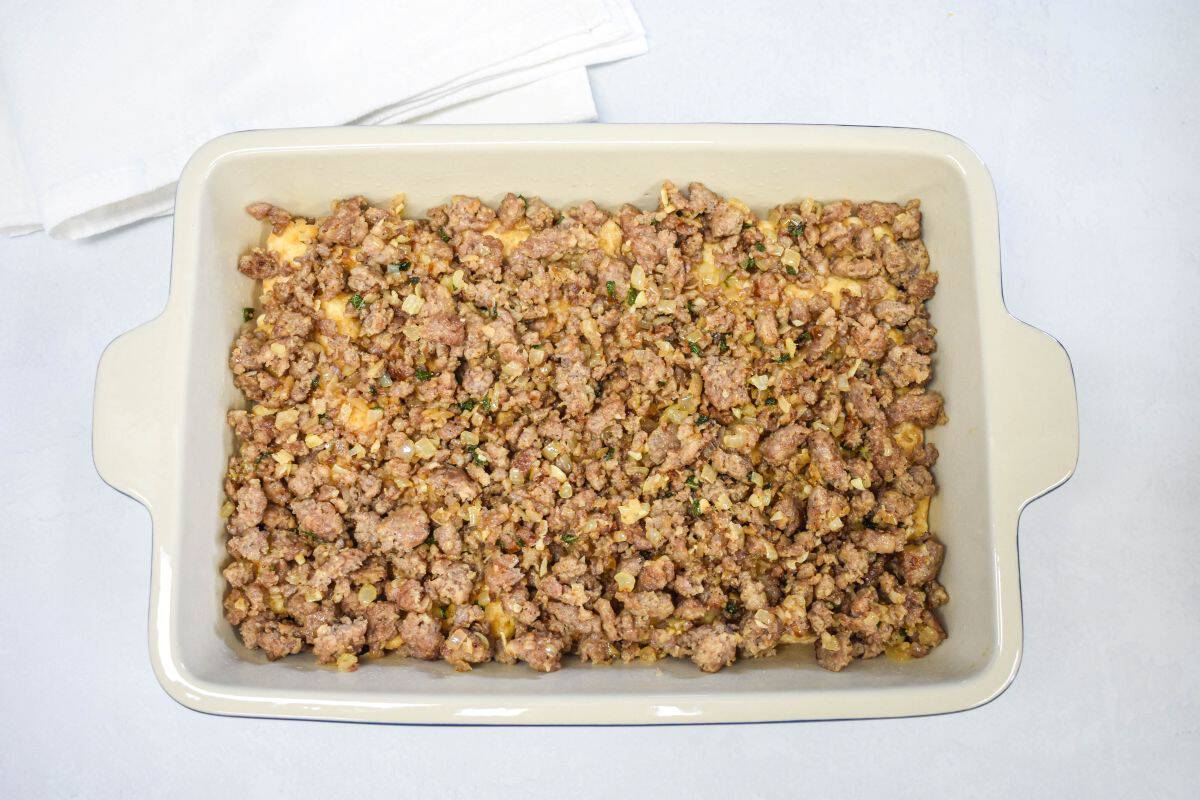 Cooked sausage mixture layered over tater tots in a baking dish.