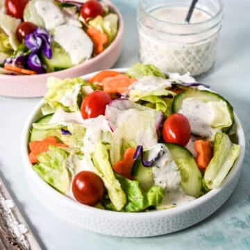 Bowls of green salad topped with parmesan peppercorn dressing, with a jar of dressing in the background.