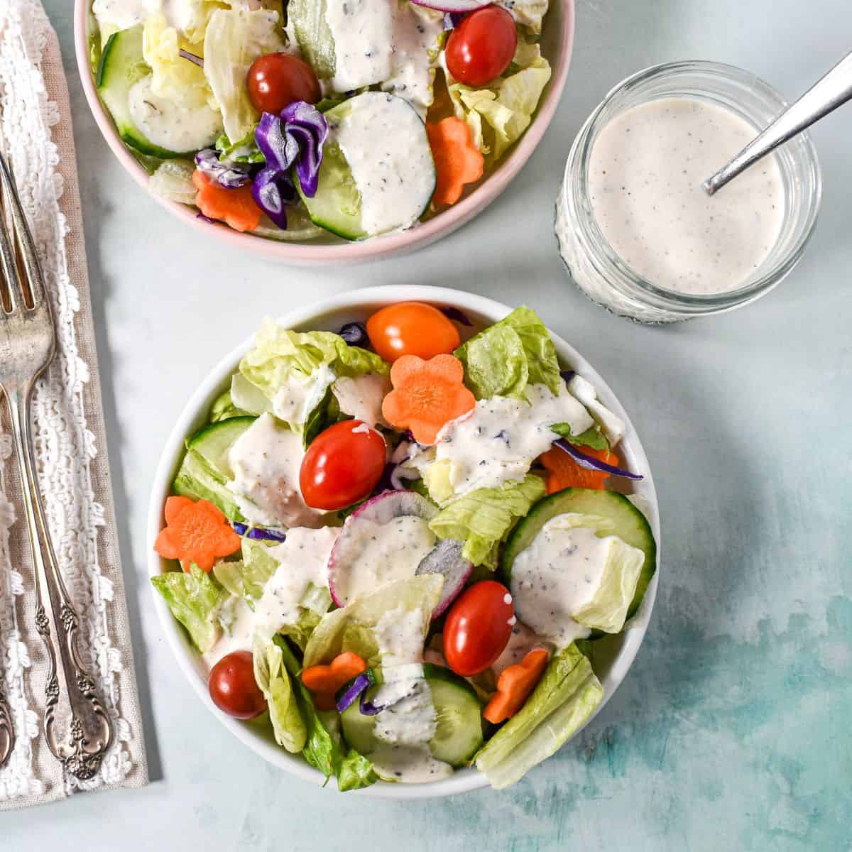 Overhead view of two green salads served with parmesan peppercorn dressing and a jar of dressing on the side.