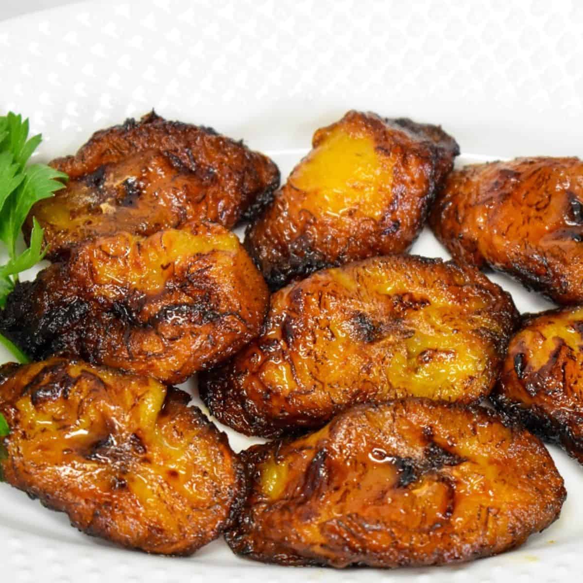The fried plantains arranged on a white plate with parsley as a garnish on the left side.