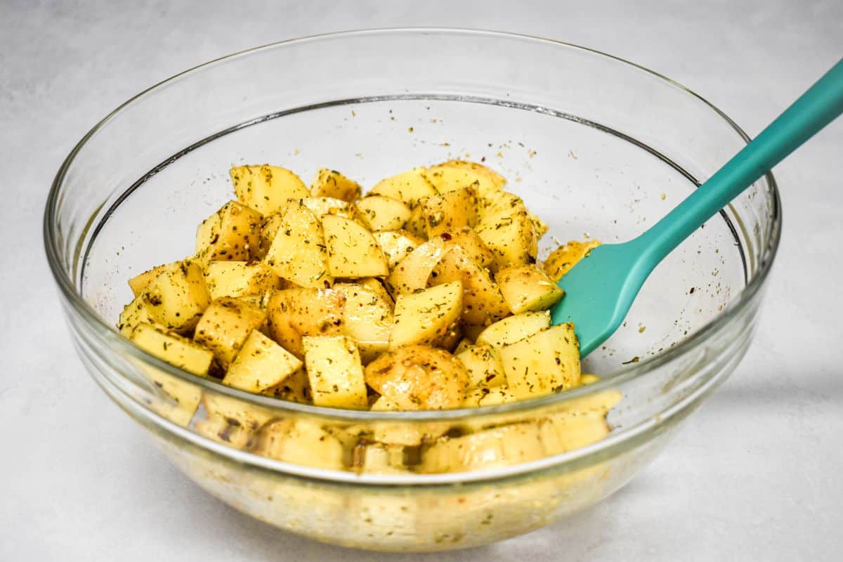 Gold potatoes tossed with oil and seasonings in a glass bowl.