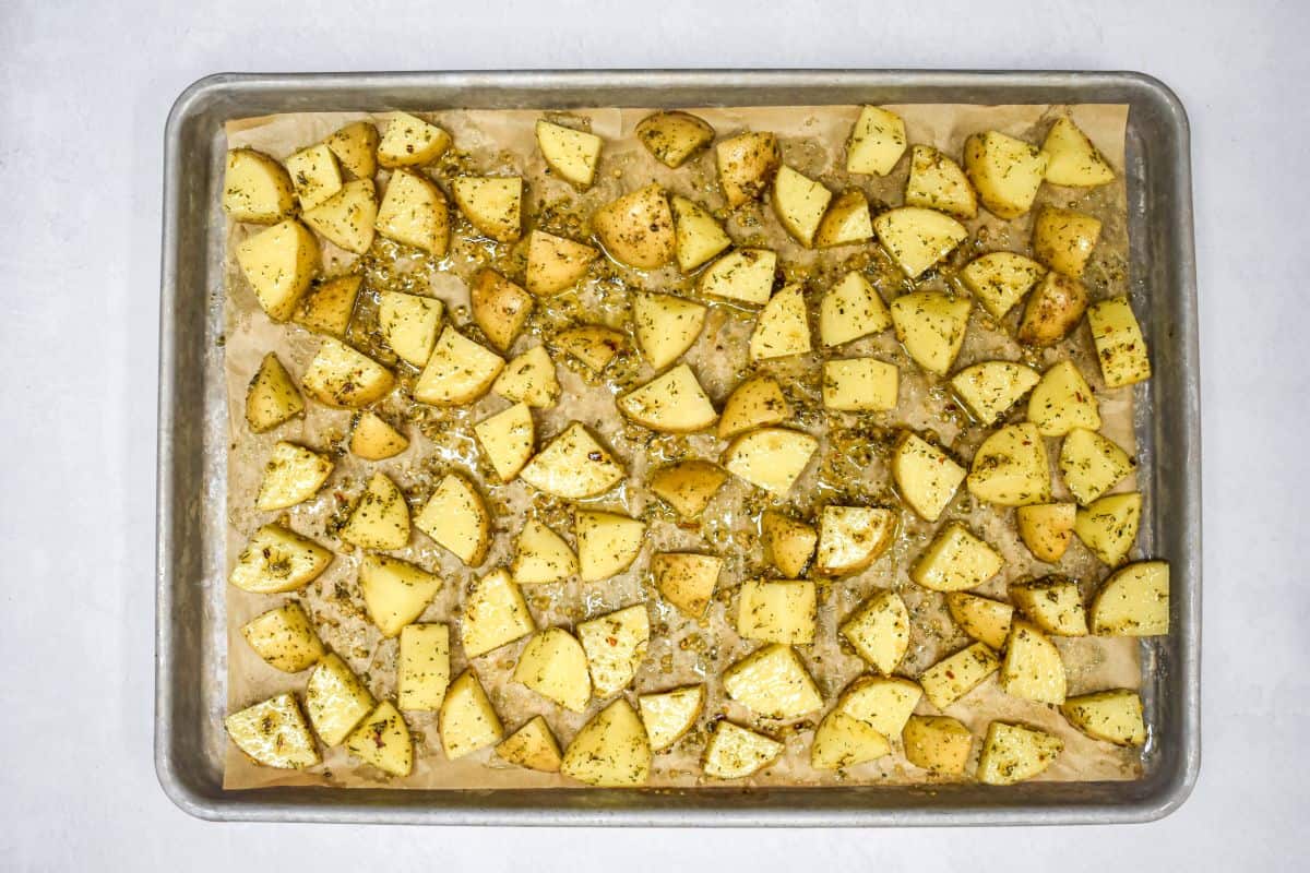 Seasoned potatoes spread in a single layer on a parchment-lined baking sheet.