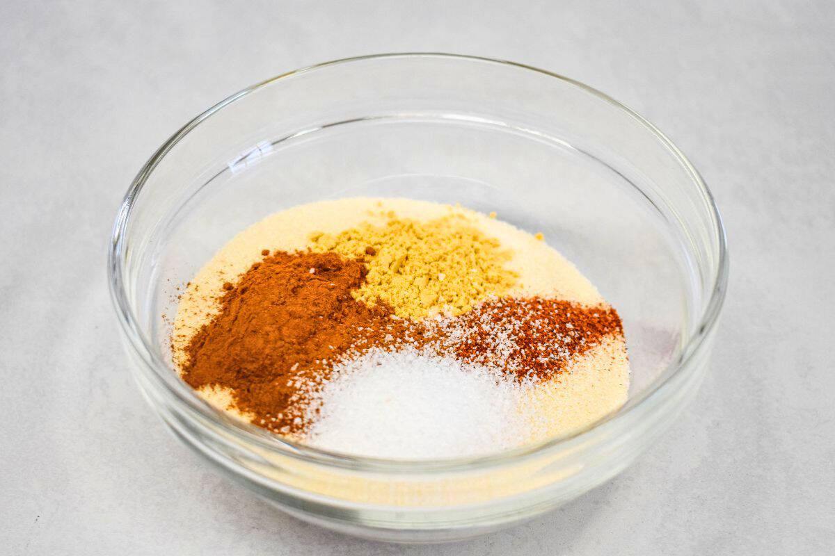 Glass bowl containing measured granulated sugar, ground cinnamon, ginger, cayenne pepper, and kosher salt, ready to mix.