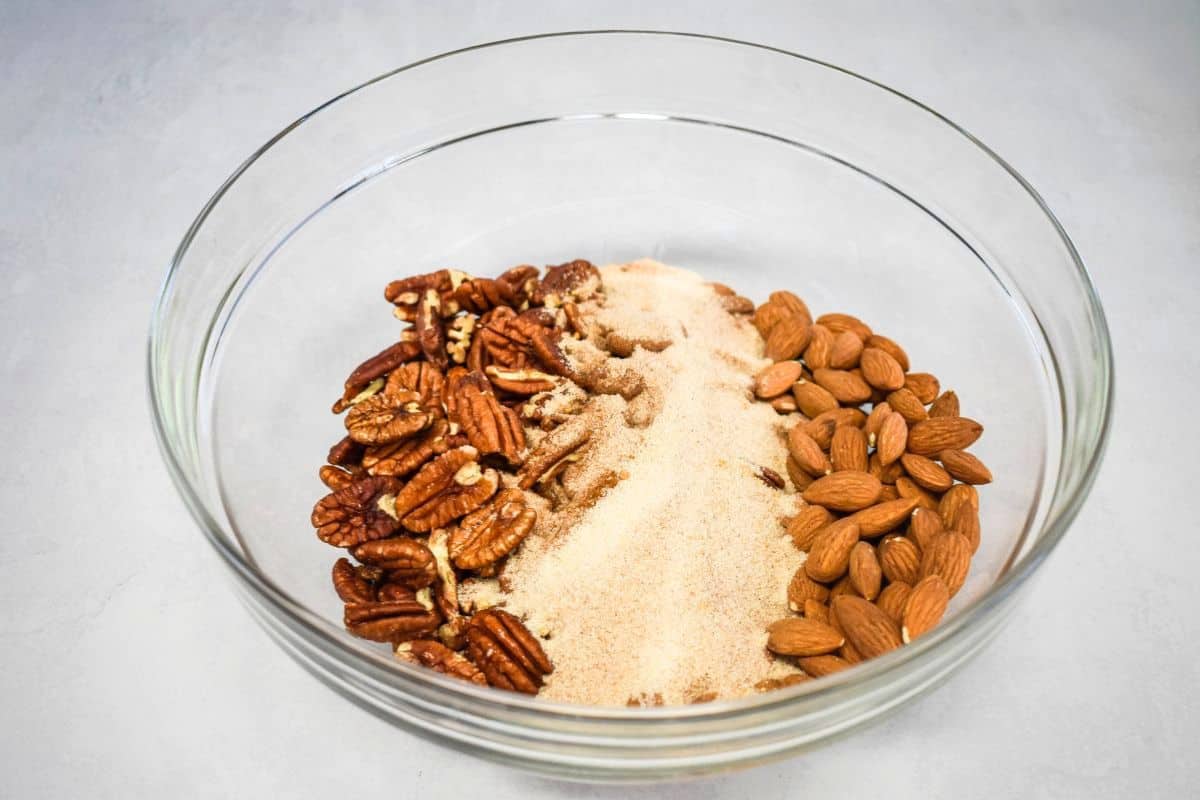 Glass bowl with raw pecan halves, raw almonds, and sugar-spice mixture before combining.