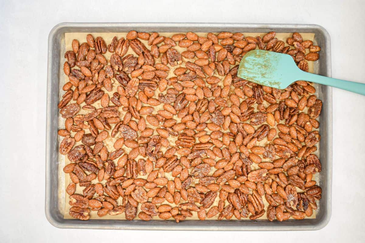 Nuts spread in a single layer on a parchment-lined baking sheet, with a teal spatula.