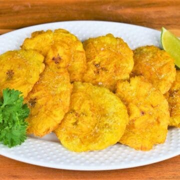 Tostones Flattened and Fried and arranged on a white plate.