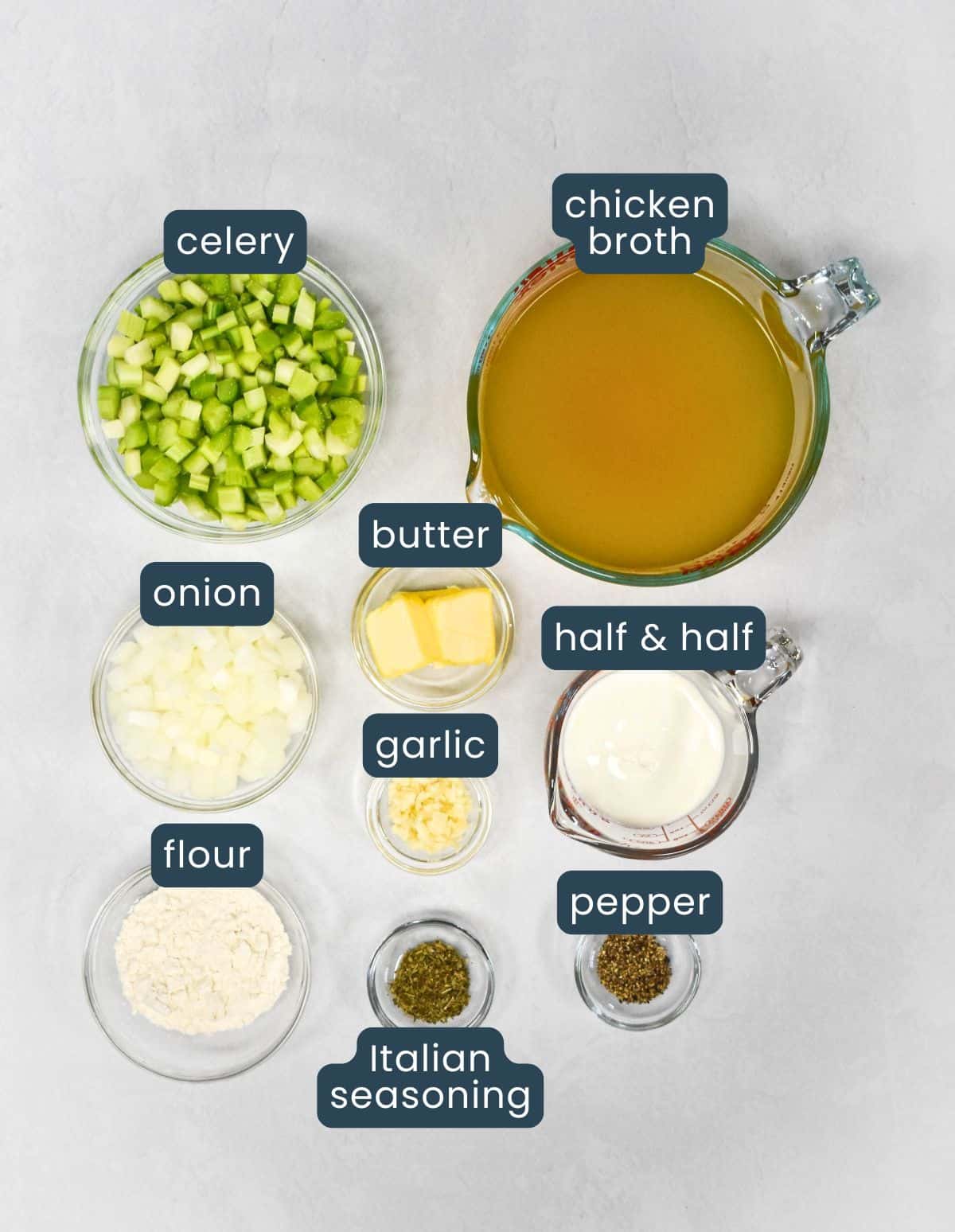 Top-down picture of the ingredients for cream of celery soup prepped and in glass bowls, including celery, onion, butter, garlic, flour, Italian seasoning, black pepper, a measuring cup of chicken broth, and a measuring cup of half-and-half, with each labeled.