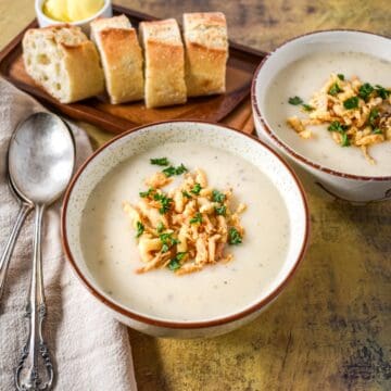 Cream of onion soup topped with crispy fried onions and parsley, served in two white bowls with sliced bread and butter on a wooden board.