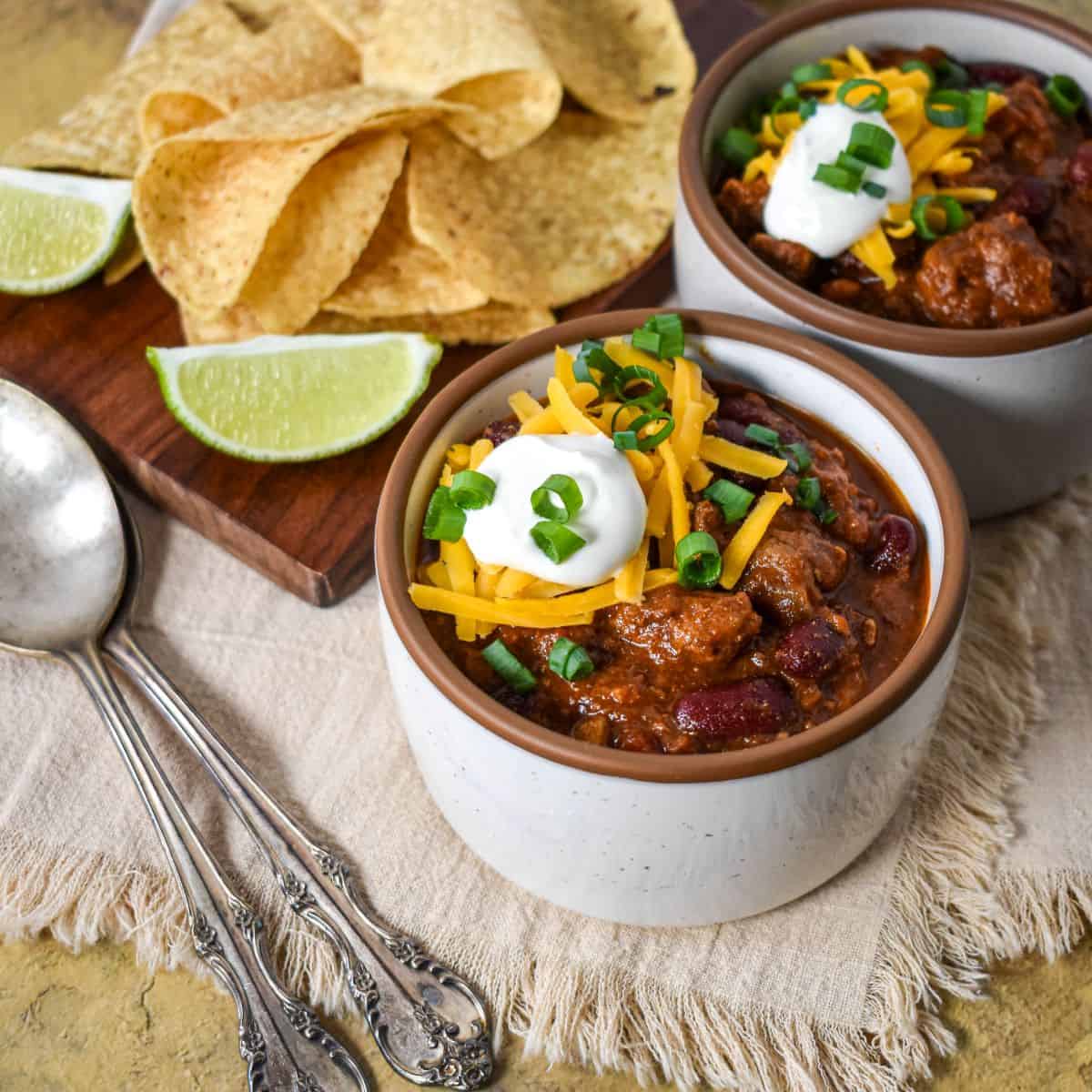 A bowl of homemade steak chili with beef and red beans, finished with cheddar cheese, sour cream, and sliced green onions.