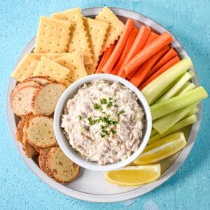 Canned salmon salad with crackers, bagel chips, carrot and celery sticks, and lemon wedges.