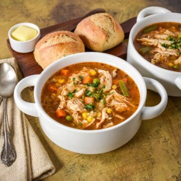 Chicken vegetable soup with shredded chicken breast, mixed vegetables, and pastina in a flavorful broth, served with crusty bread.