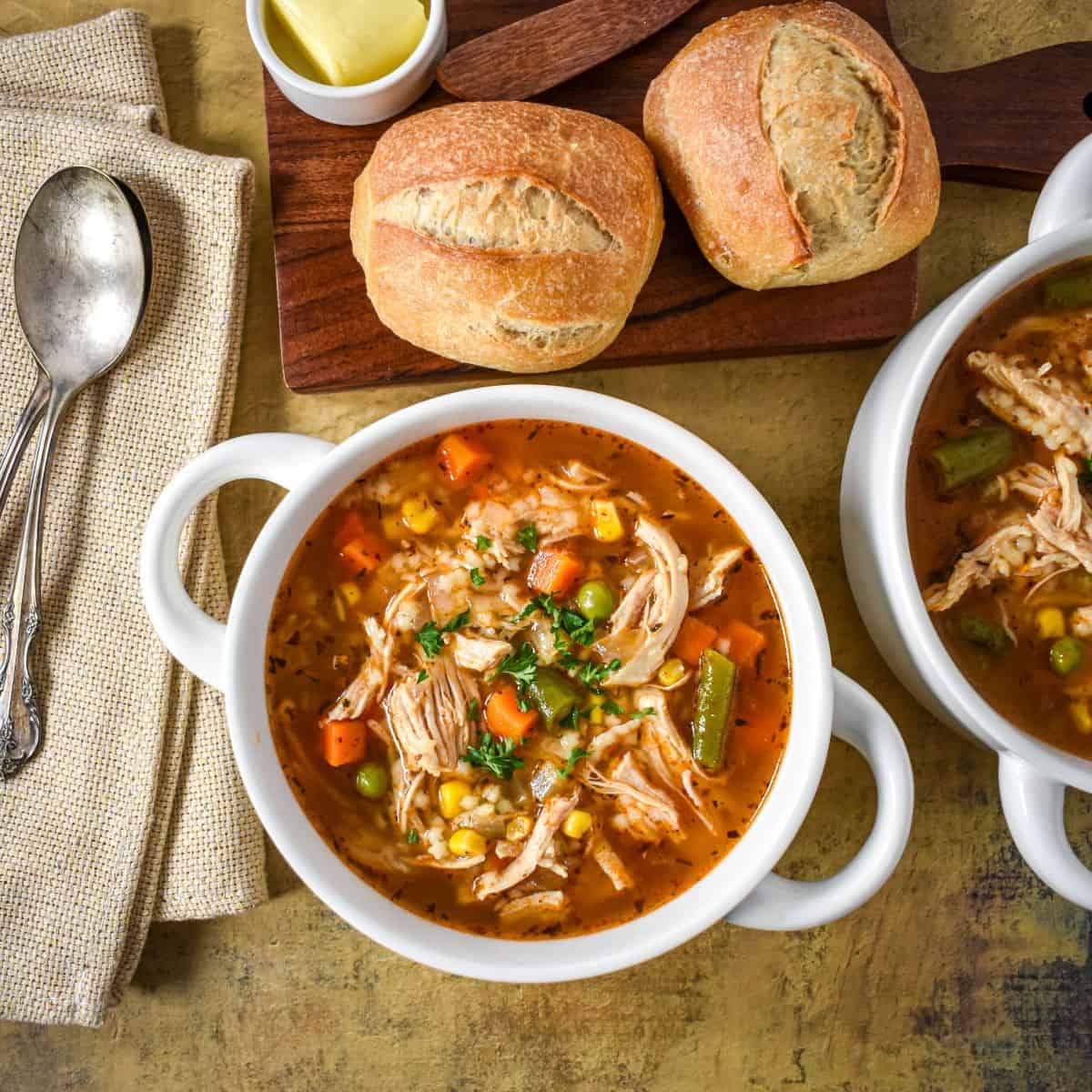 Overhead close-up of a bowl of soup loaded with tender shredded chicken, colorful vegetables, and small pasta, garnished with fresh parsley.